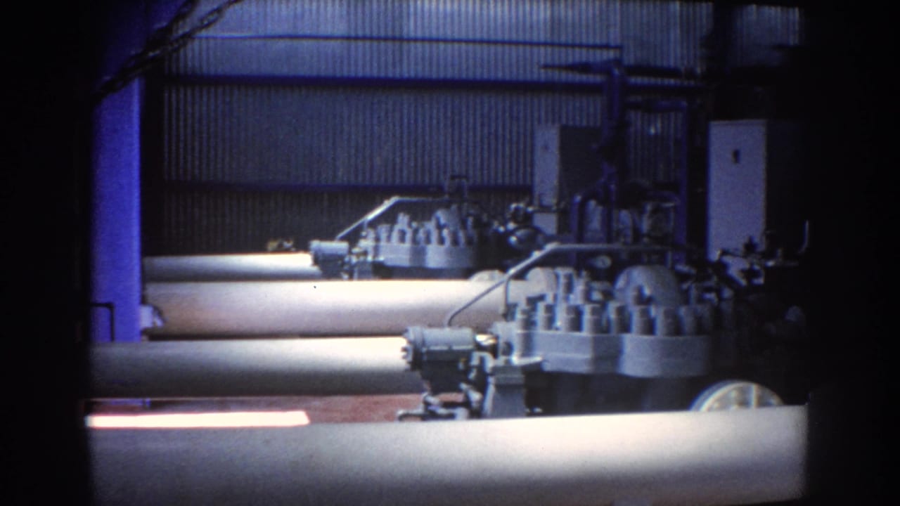 Industrial interior with large pipes, valve housings, and corrugated metal wall panels.