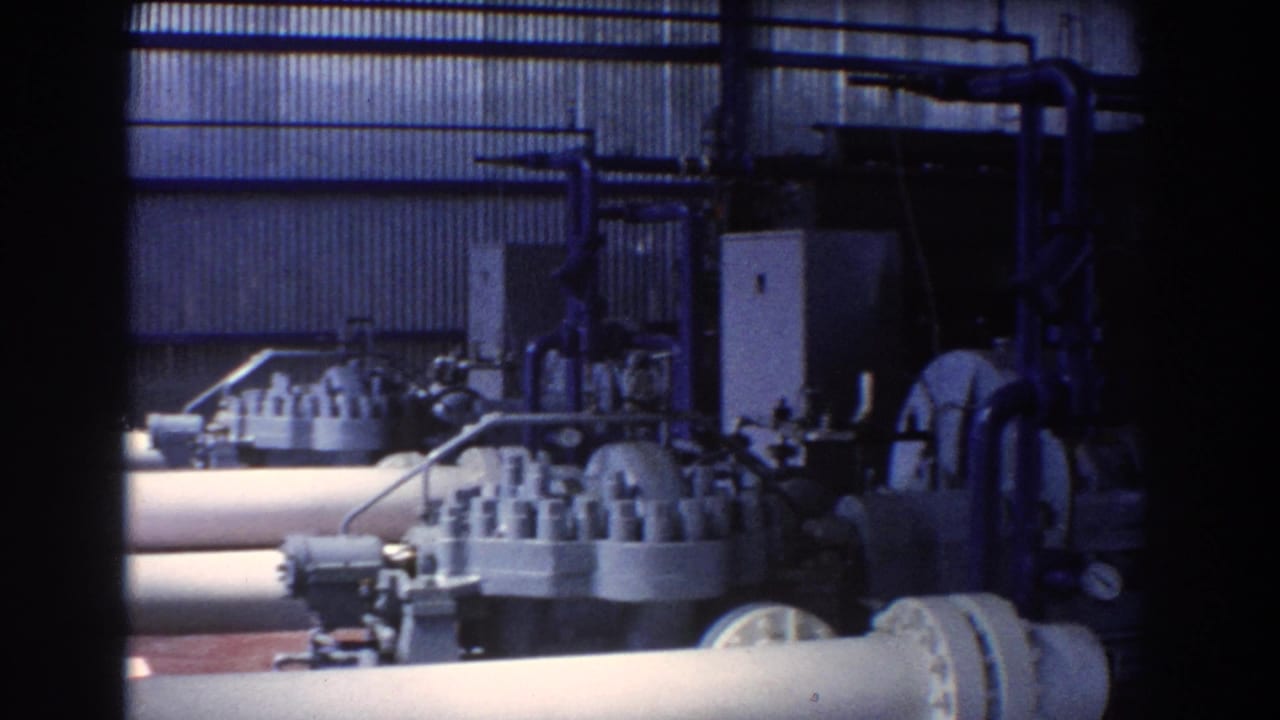 Industrial machinery seen behind a large pipe and dark vertical frame edge.