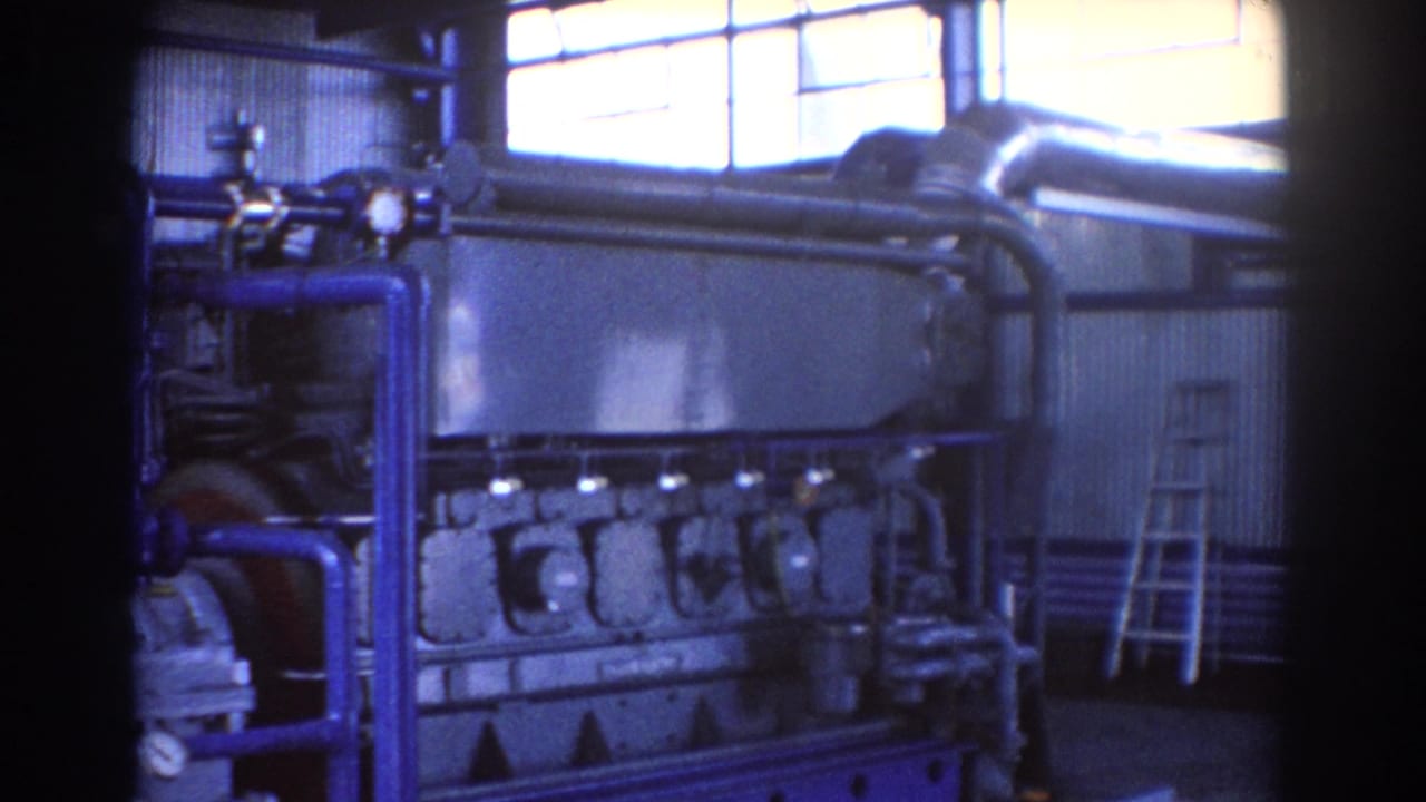 1967 Brisbane 8mm frame showing a large industrial engine, blue pipework, high windows, and a ladder inside a factory or power-plant room.