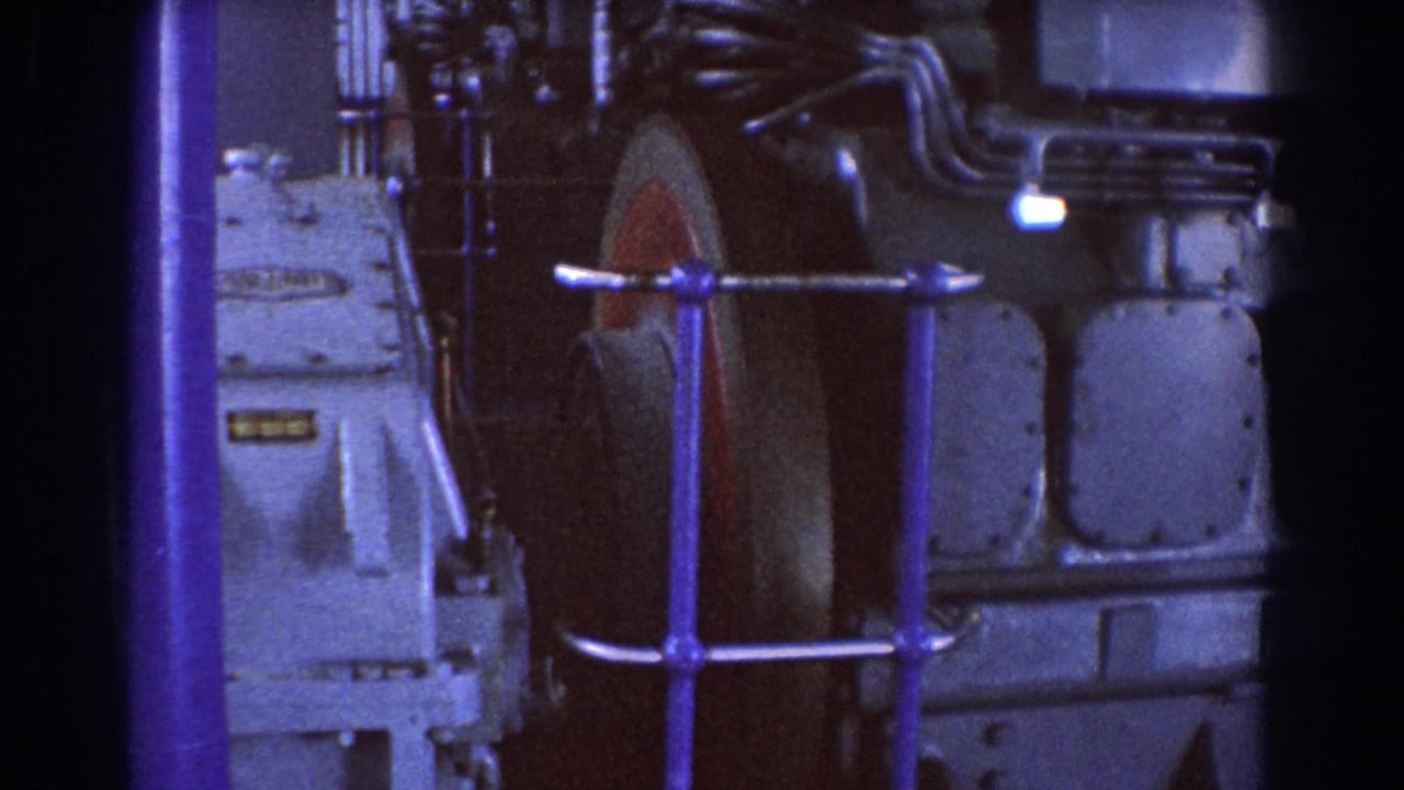 1967 Brisbane 8mm frame showing a large industrial machine, blue railing, bolted panels, and pipes in a factory interior.