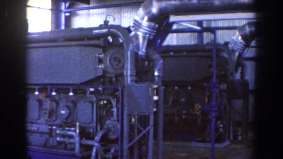 1967 Brisbane factory frame with blue supports, large machinery, diagonal pipework, and shadowed industrial space.