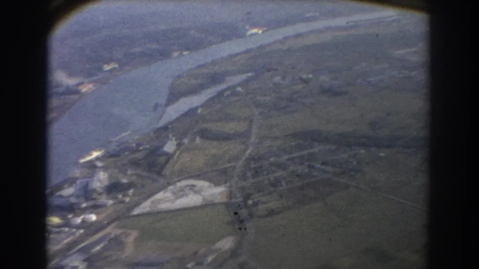 1967 Brisbane aerial view from an aircraft, showing a broad waterway, shoreline, fields, and indistinct developed areas below.