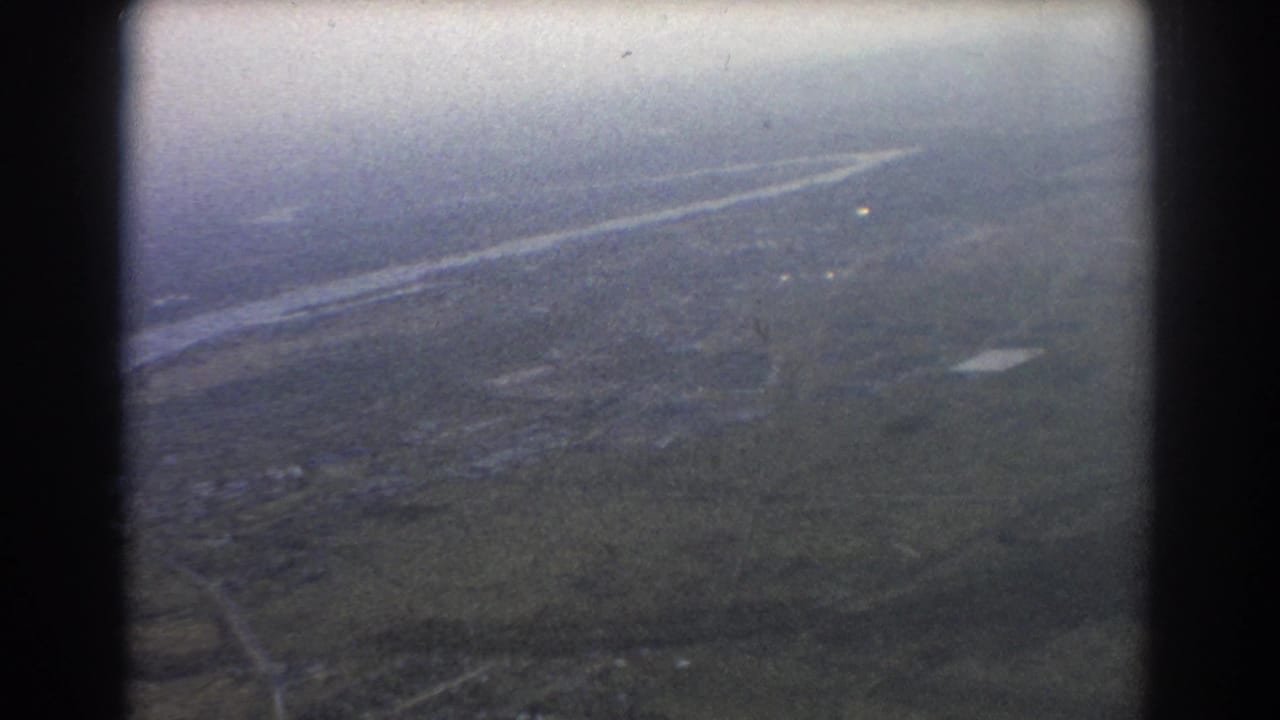 Hazy aerial view of land and water seen through an airplane window.
