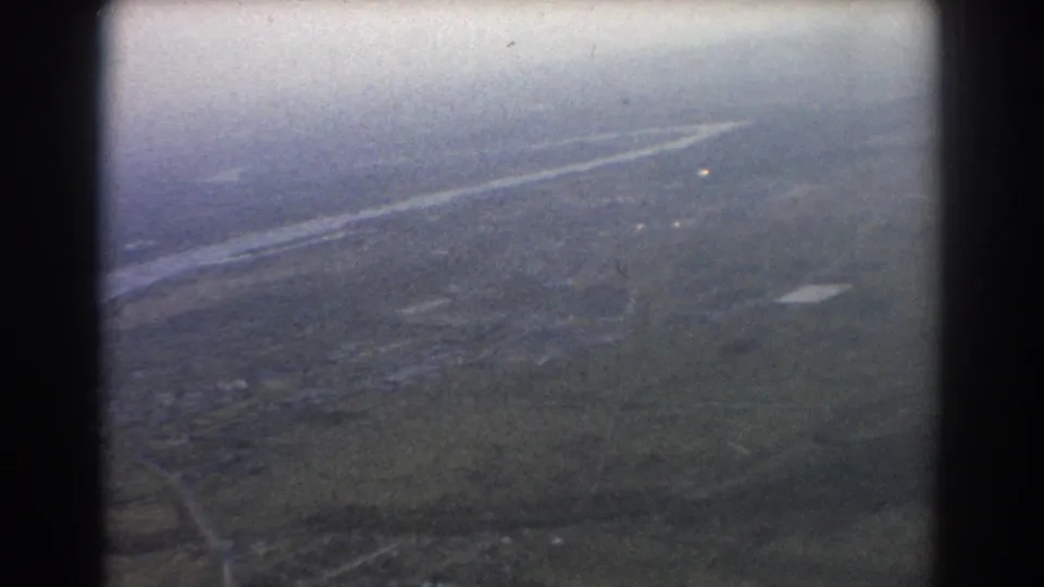 1967 8mm frame showing a hazy aerial view over terrain and a winding watercourse, supported by Brisbane, Australia clip metadata.