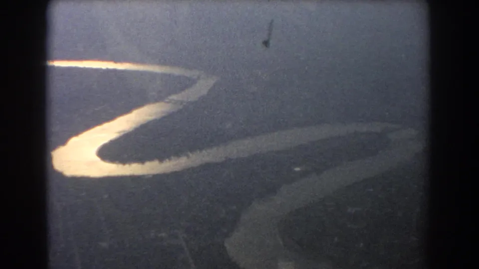 1967 aerial home-movie view near Brisbane showing a sunlit winding river cutting through darker terrain below.