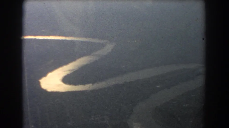Aerial 8mm frame from the Brisbane travel clip showing a bright river bend and surrounding dark land from a plane.