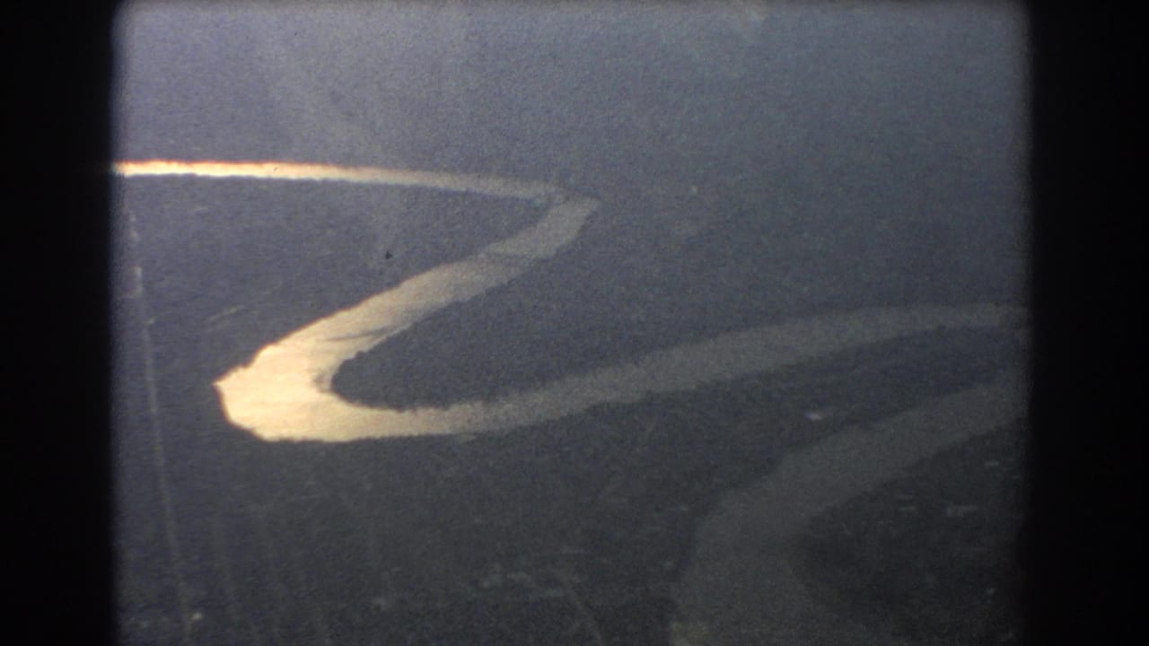 Winding sunlit river seen through a dark aircraft window frame.