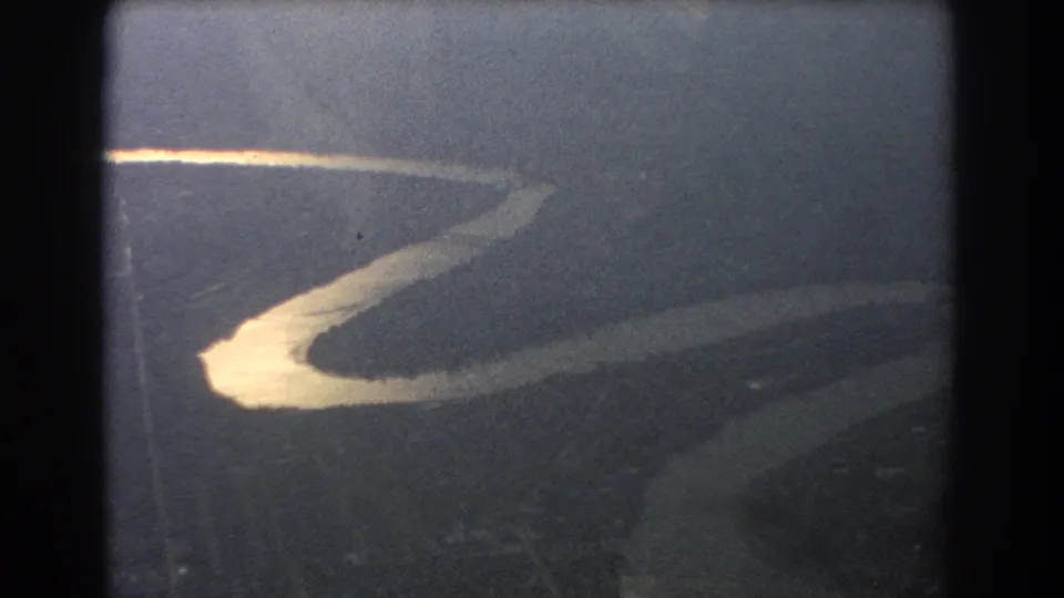 1967 Brisbane-area 8mm frame showing a bright curving river below, viewed through an aircraft window with grain and haze.