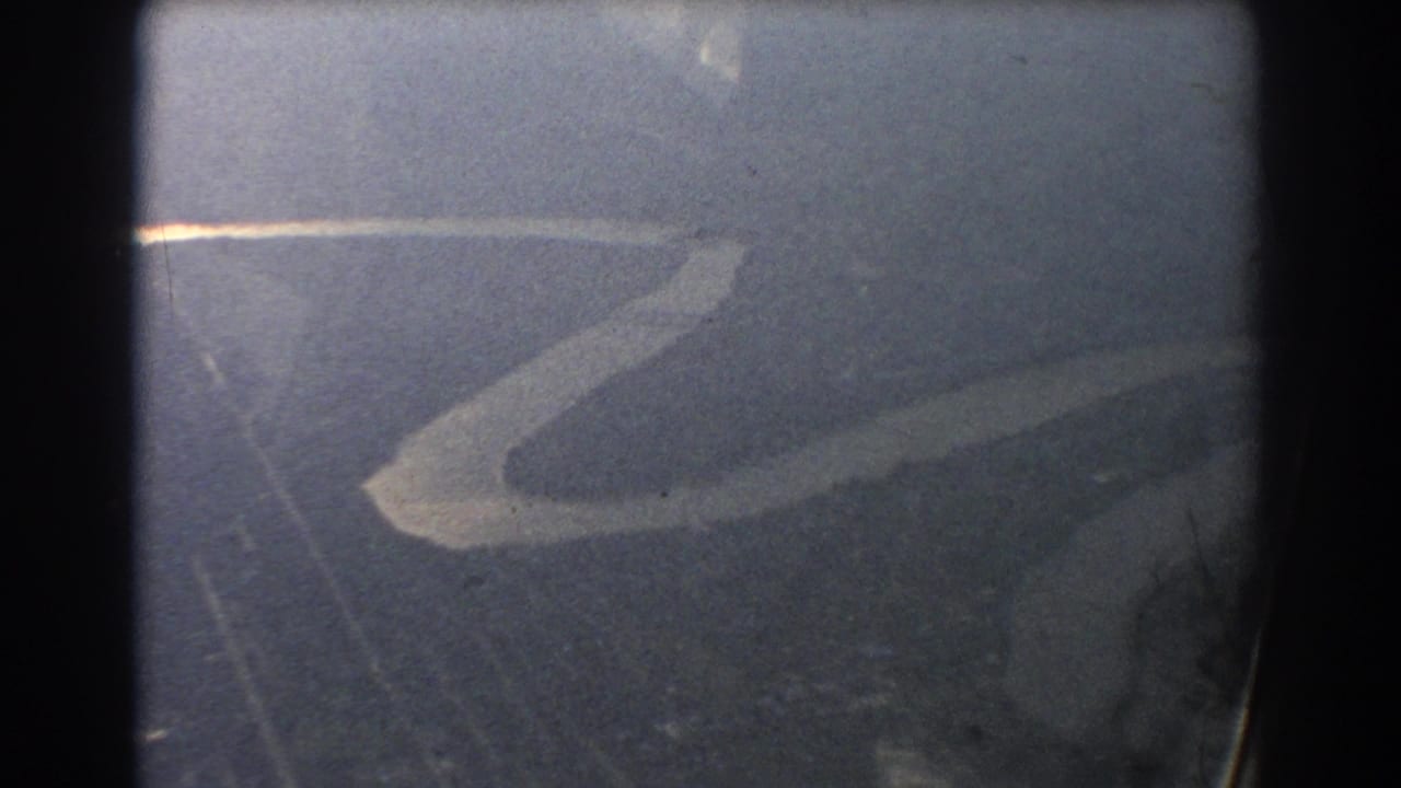 Soft aerial view of a winding pale river or shoreline through dark 8mm frame edges.