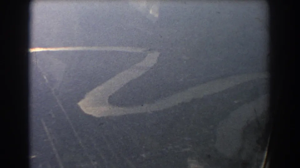 1967 8mm frame showing a soft aerial view of a winding river or shoreline, with visible film grain and dark gate edges.