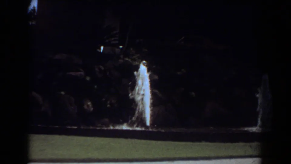 1967 Fort Lauderdale home-movie frame showing two fountain sprays in a nighttime landscaped park setting.