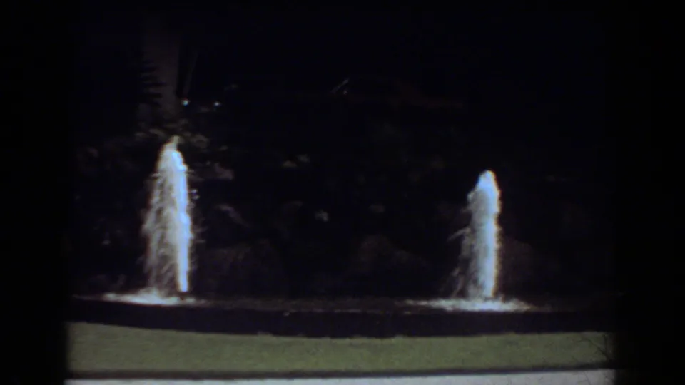 1967 Fort Lauderdale frame of two illuminated fountain jets over a lawn and dark landscaped background.