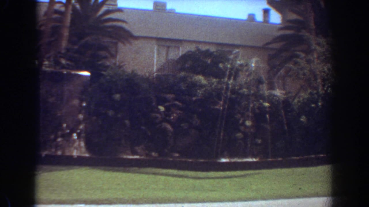 1967 Fort Lauderdale home-movie frame showing a residence and front-yard fountain partly obscured by motion blur and a passing white car.