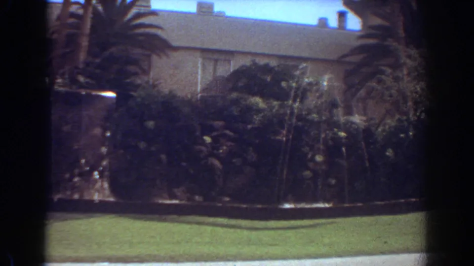 1967 Fort Lauderdale home-movie frame showing a residence and front-yard fountain partly obscured by motion blur and a passing white car.