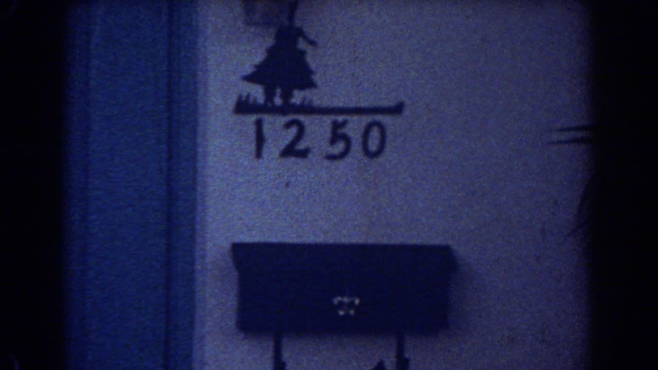 Close 1967 home-movie frame showing the number 1250 on a wall above a dark mailbox, with heavy grain and shadow.