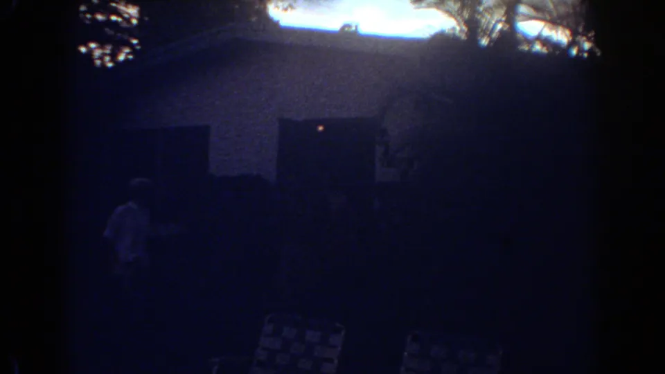 Fort Lauderdale home-movie frame with a small person near the house, patio chairs, trees, and a bright backlit sky.