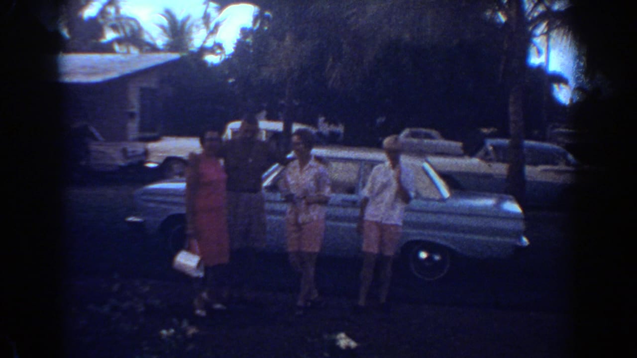 Family members pose by a sedan in a 1967 Fort Lauderdale home-movie frame with palms and parked cars in the background.