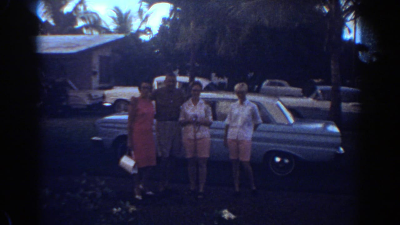 Four adults face the camera near a light blue car in Fort Lauderdale, with palms and parked cars behind them.