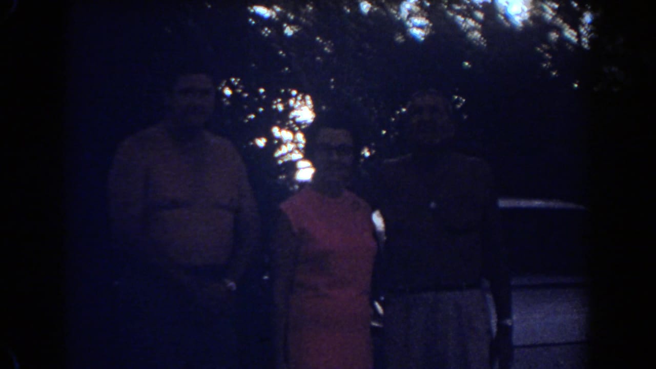 Three adults in Fort Lauderdale stand in a closer, darker view, with tree canopy and part of a car behind them.