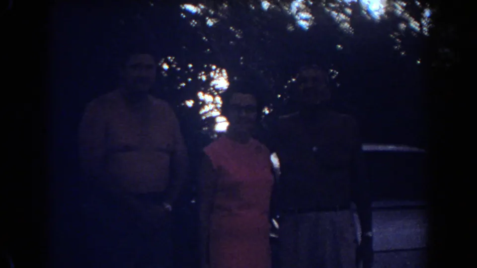 Three adults in Fort Lauderdale stand in a closer, darker view, with tree canopy and part of a car behind them.