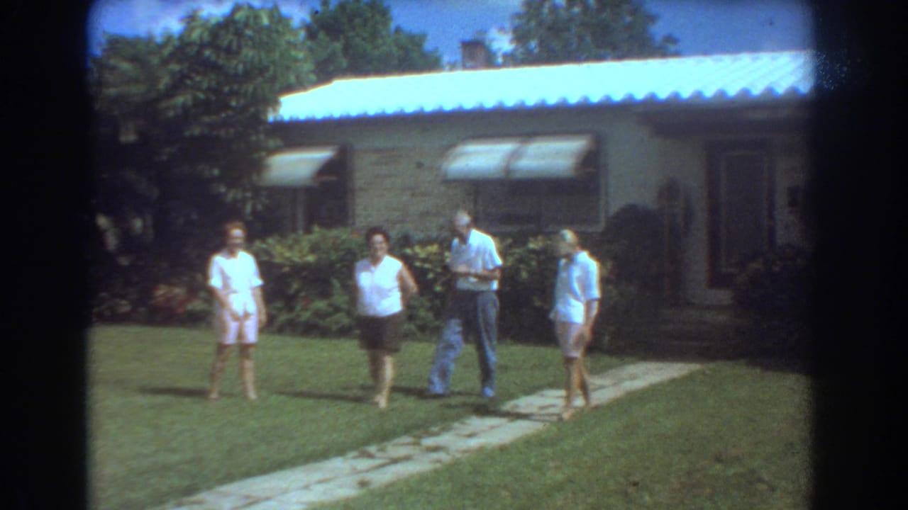 In 1967 Fort Lauderdale, four older adults move casually across a suburban yard outside a brick house with awnings.