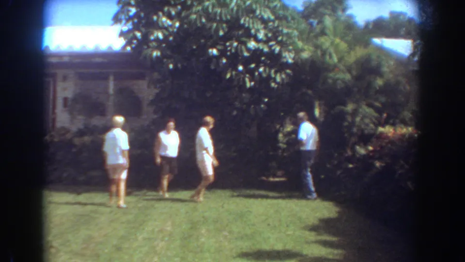 A small group of adults walks through a Fort Lauderdale residential yard, with tropical foliage and a house exterior in the background.
