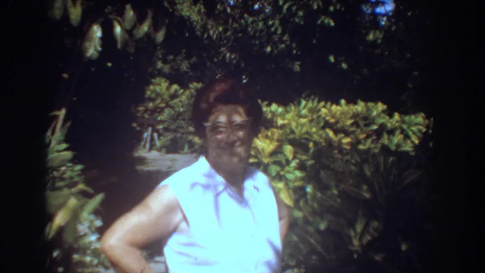 In 1967 Fort Lauderdale home-movie footage, a woman in glasses and a white sleeveless shirt faces the camera in a lush garden.