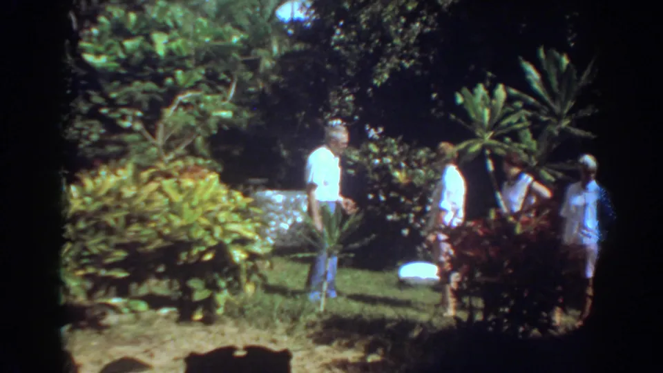 Several adults appear among tropical shrubs and trees in a sunlit Fort Lauderdale garden scene from 1967 home-movie footage.