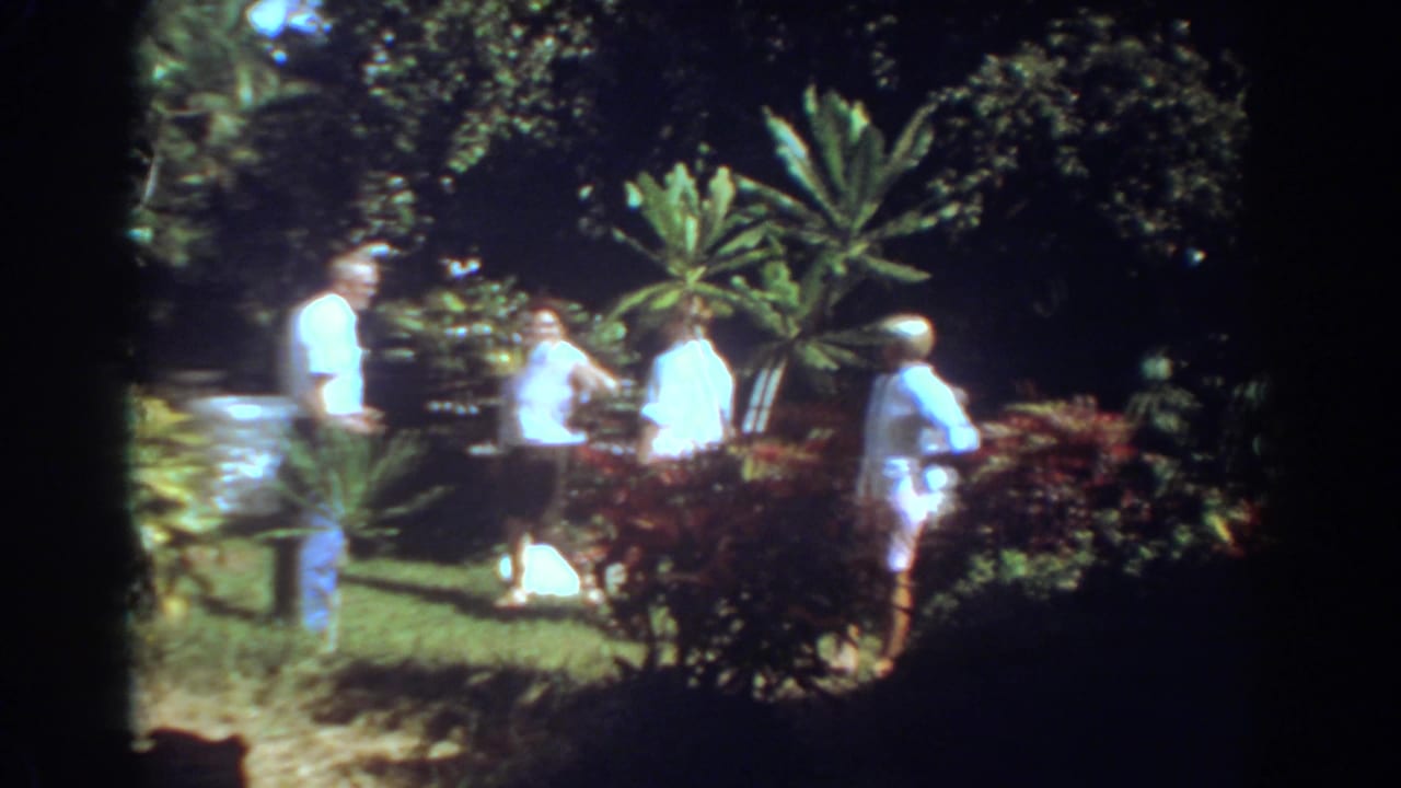 Adults in summer clothing stand in a Fort Lauderdale tropical garden, with a white object visible on the lawn nearby.