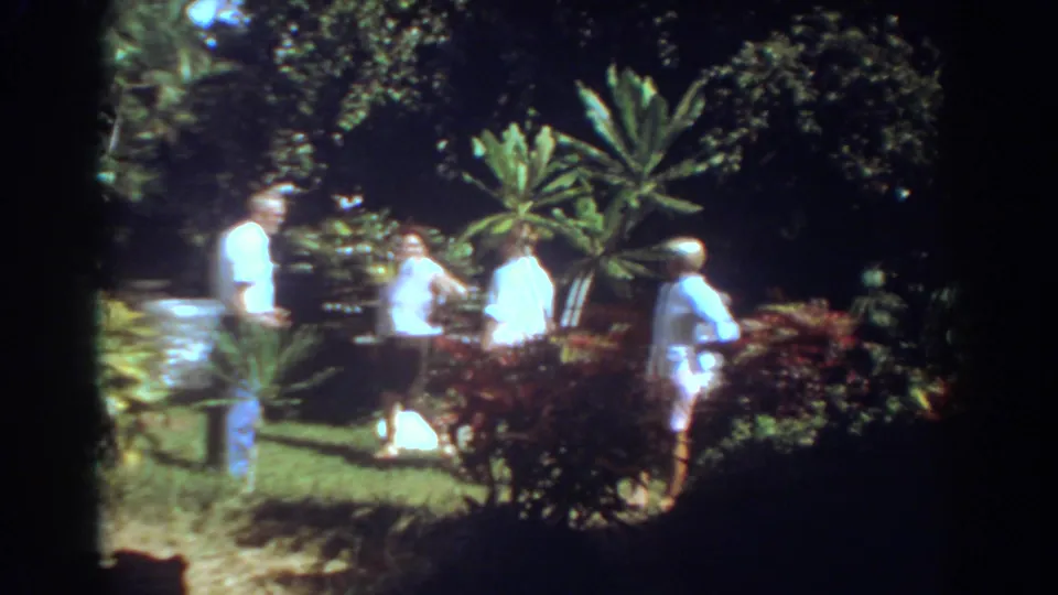 Adults in summer clothing stand in a Fort Lauderdale tropical garden, with a white object visible on the lawn nearby.