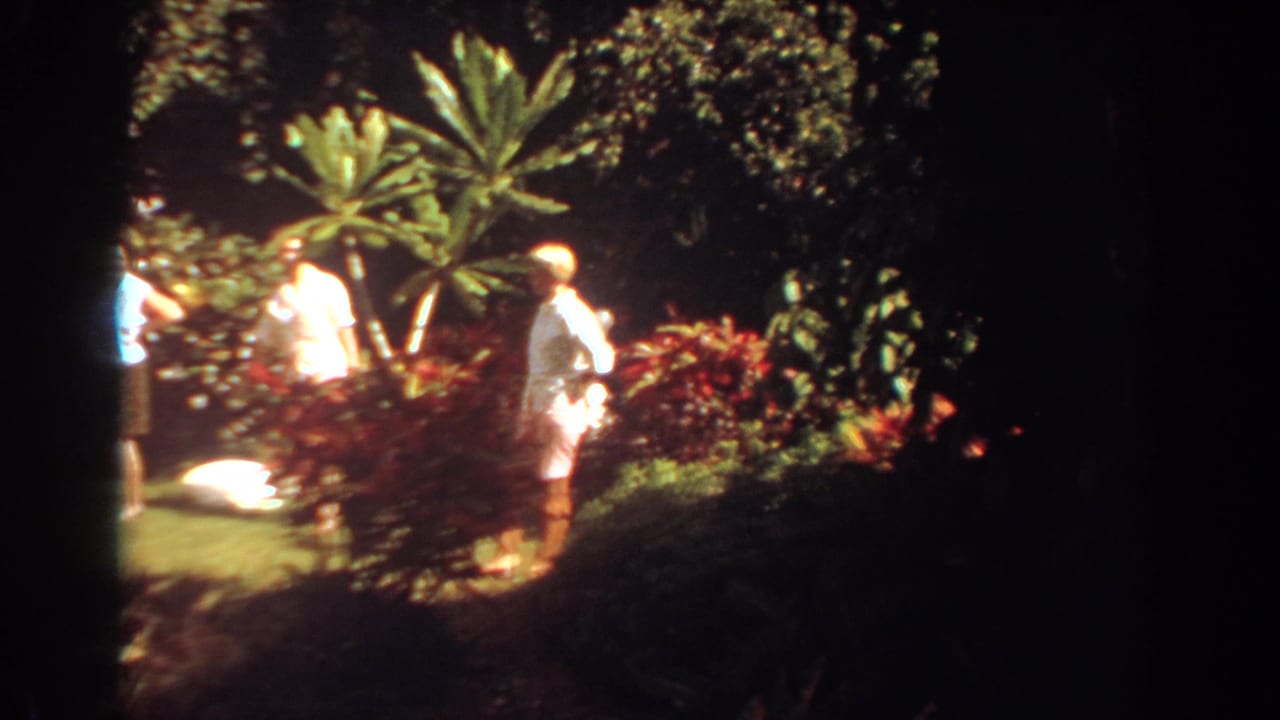 A woman in black shorts crosses a sunny tropical garden scene in Fort Lauderdale while others continue walking nearby.