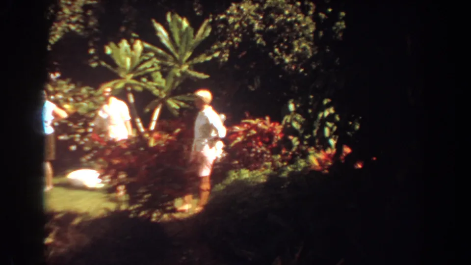 A woman in black shorts crosses a sunny tropical garden scene in Fort Lauderdale while others continue walking nearby.