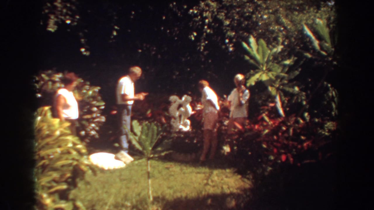 The home-movie frame shows adults near a landscaped garden feature in 1967 Fort Lauderdale, with dense tropical planting around them.