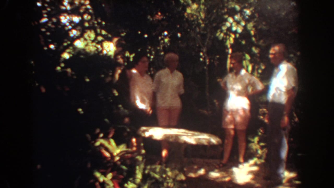 Four adults in light warm-weather clothing stand near foliage and a stone table in Fort Lauderdale archival home-movie footage.