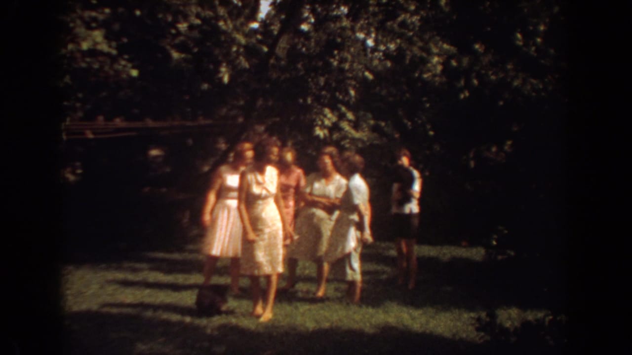 Group of women in light dresses standing on a shaded grassy lawn.