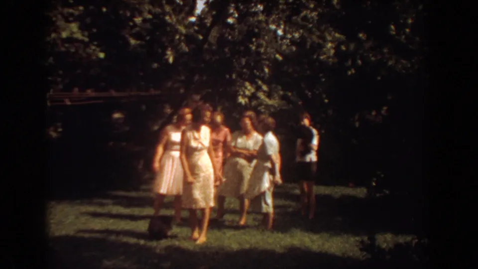 1967 Fort Lauderdale home-movie frame showing women in pale dresses gathered under trees on a lawn.
