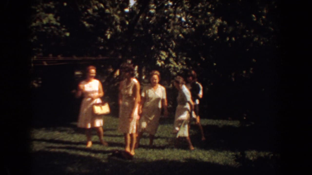 A candid 1967 home-movie frame shows women with handbags walking and talking on a lawn in Fort Lauderdale.