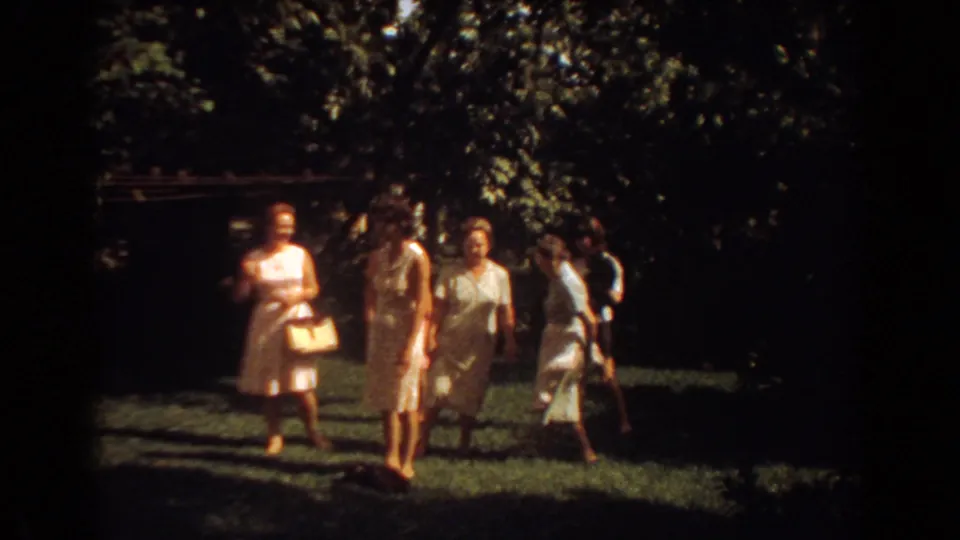 A candid 1967 home-movie frame shows women with handbags walking and talking on a lawn in Fort Lauderdale.