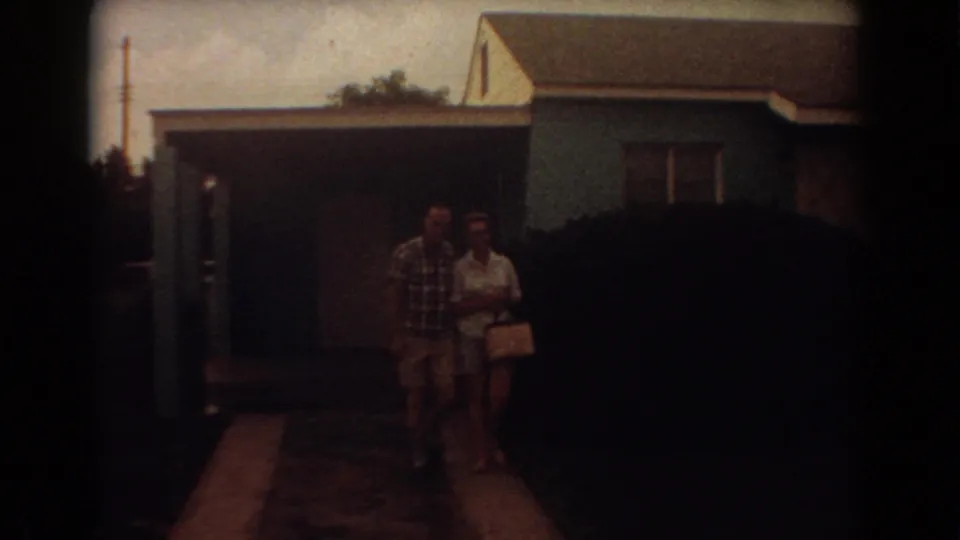The couple walks arm-in-arm toward the camera outside a blue Fort Lauderdale house in 1967 home-movie footage.