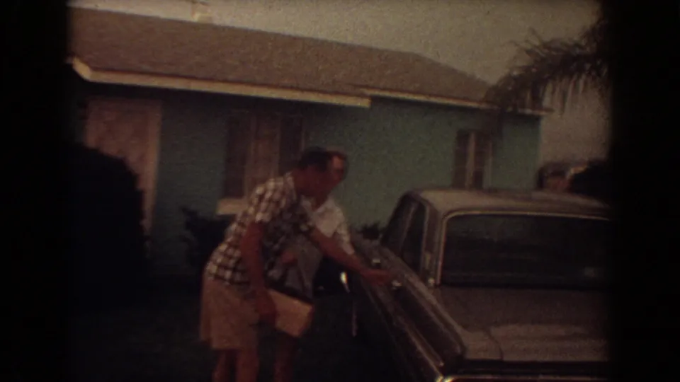 The couple reaches the dark car outside the Fort Lauderdale house, with another pale car visible nearby.