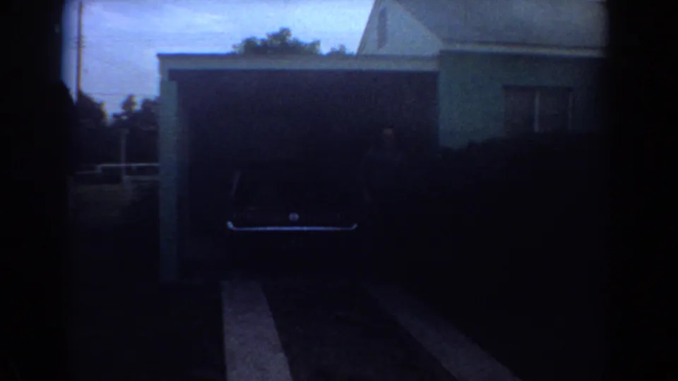 A dim view shows the dark garage opening, driveway, and part of the light blue Fort Lauderdale house.