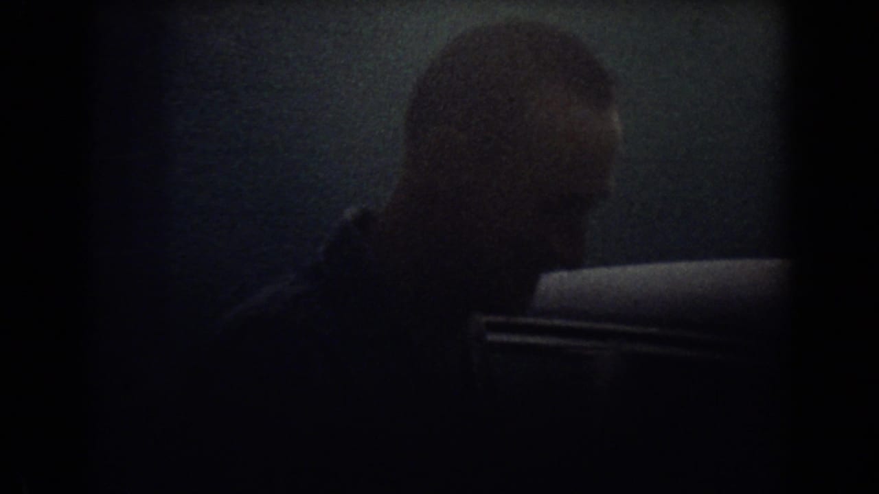 A man is seen in profile beside a parked car during a dim 1967 Fort Lauderdale home-movie scene.