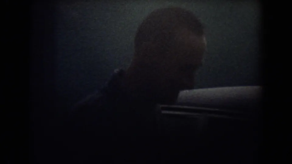 A man is seen in profile beside a parked car during a dim 1967 Fort Lauderdale home-movie scene.