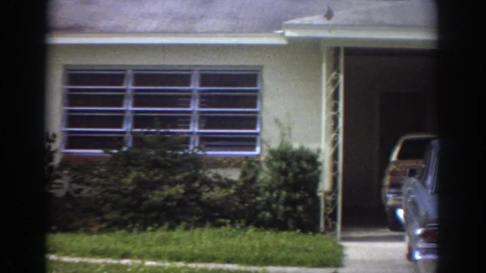 Fort Lauderdale 1967 home-movie frame showing a single-story suburban house with a louvered window, shrubs, and lawn.