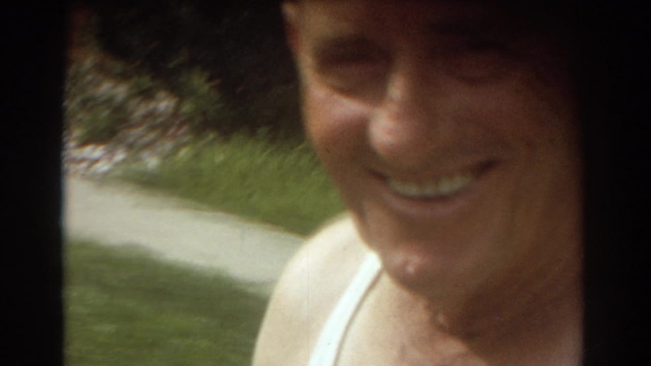 Smiling older man in a white tank top near a residential doorway.