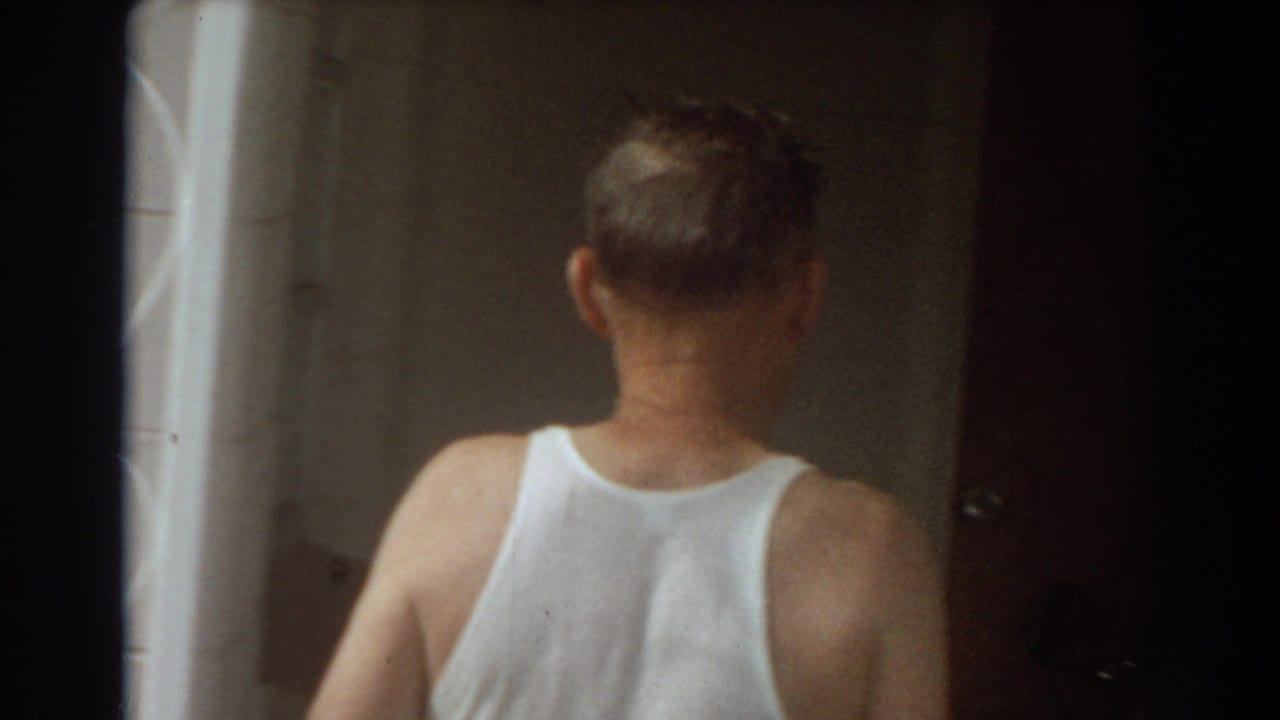 Man in a white tank top seen from behind entering a dim doorway.