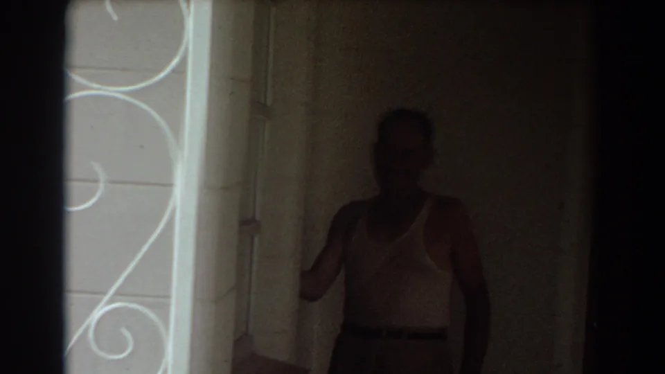 The man is silhouetted inside a dim residential space, with the bright doorway and decorative exterior detail at the edge of frame.