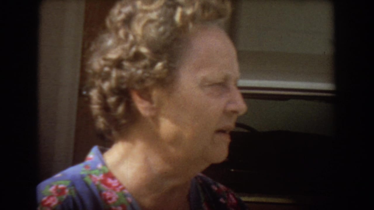 Older woman with curly light hair speaking in profile near a doorway.