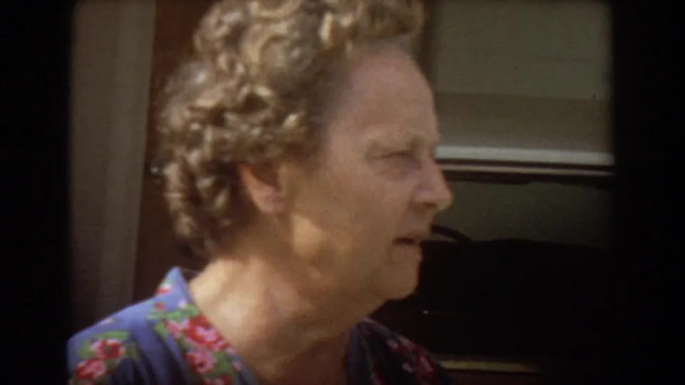 Older woman in a blue floral dress speaks in profile near a doorway in 1967 Fort Lauderdale home-movie footage.