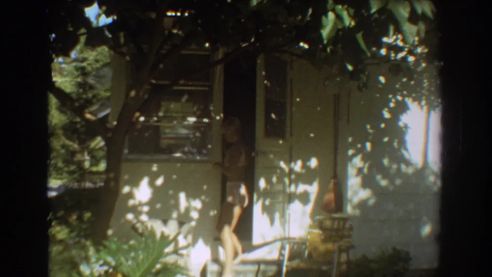 Young woman in a light swimsuit appears in the front doorway of a shaded Fort Lauderdale bungalow.